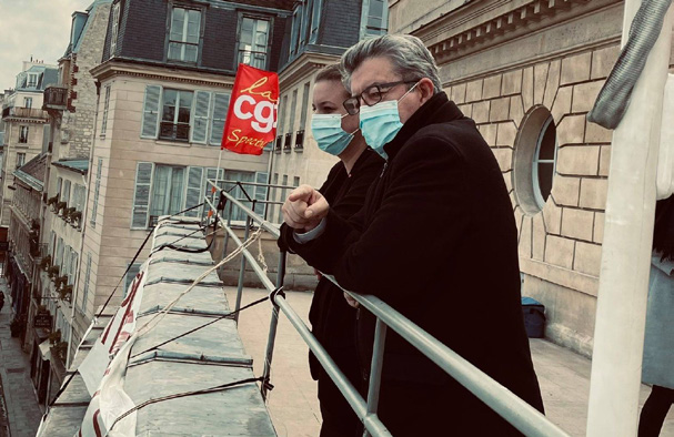Deux personnes (Mathilde Panot et Jean-Luc Mélenchon) se penchent depuis un balcon en milieu urbain, avec un drapeau CGT visible en arrière-plan et des immeubles parisiens haussmanniens.